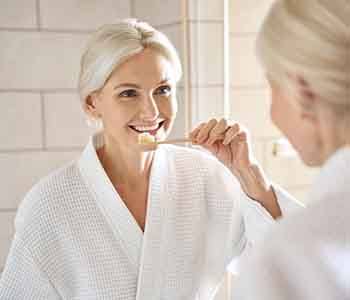 Woman smiling while brushing her teeth in bathroom