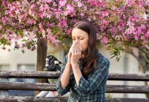 Sneezing woman sitting on bench next to flowering tree
